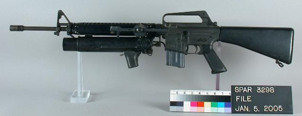 Rifle with launcher on display stand with reference ruler and color gradient plaque.  