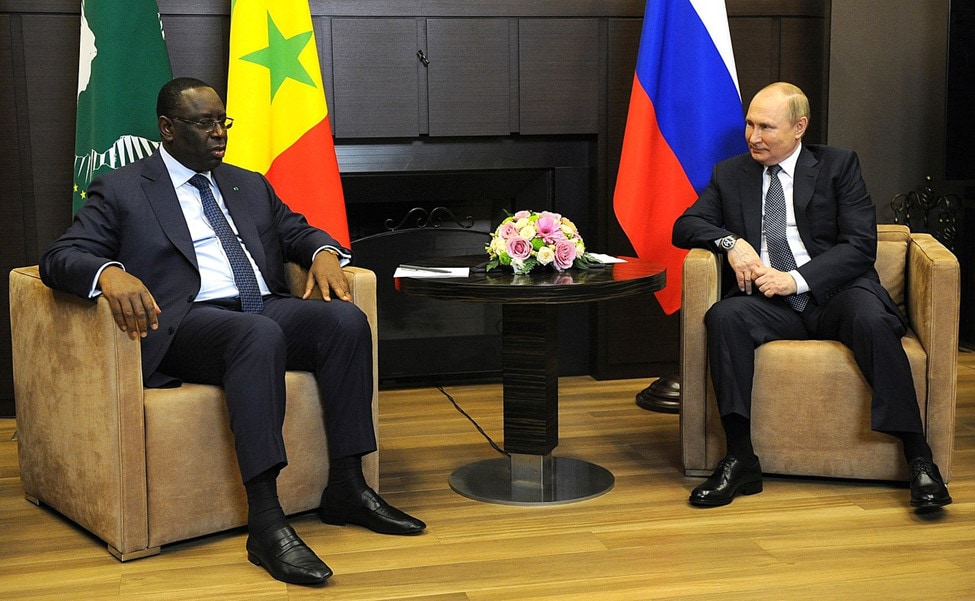 Putin and Sall sitting in Chairs with flowers between them.