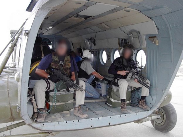 Three men with weapons in the back of a Soviet helicopter.