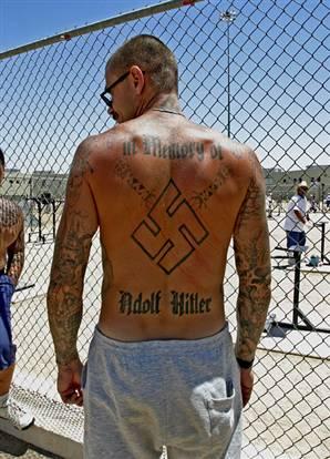 A member of the Aryan Brotherhood showing his tattoos while in a prison yard. Tributes to Adolf Hitler and the Nazi Party are signature elements. 