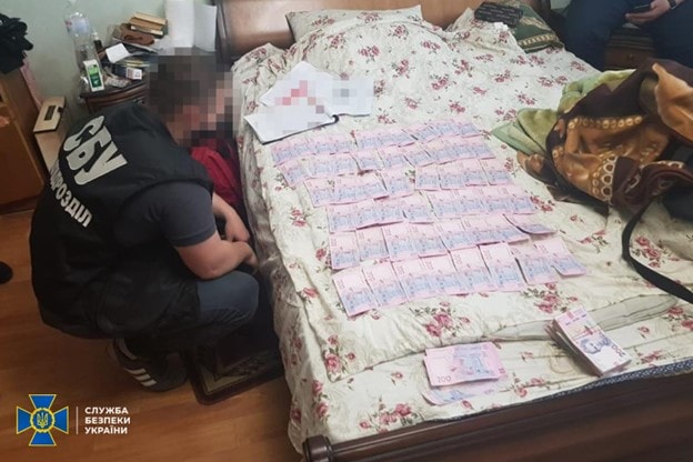 Officer looks at a bed covered in cash money.
