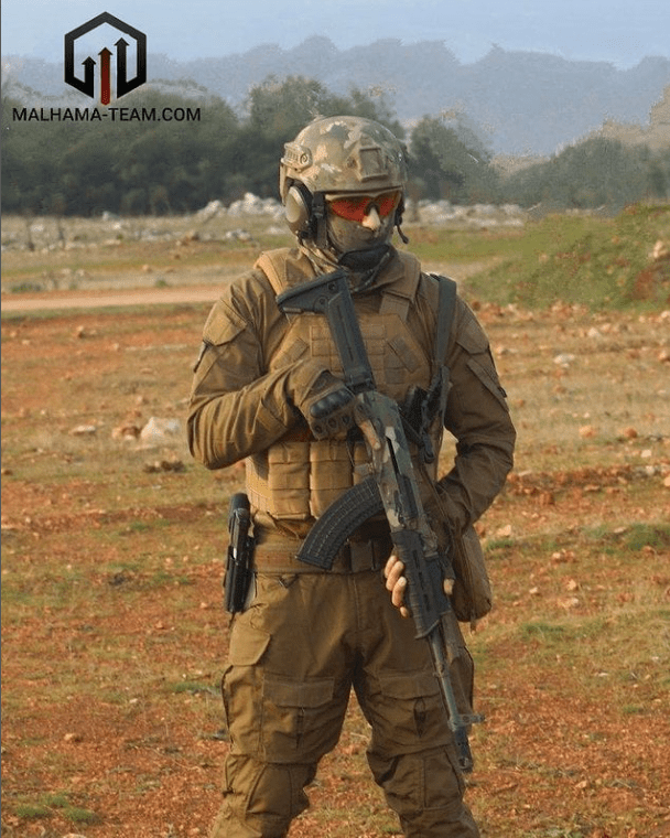 Man poses in combat gear with rifle.