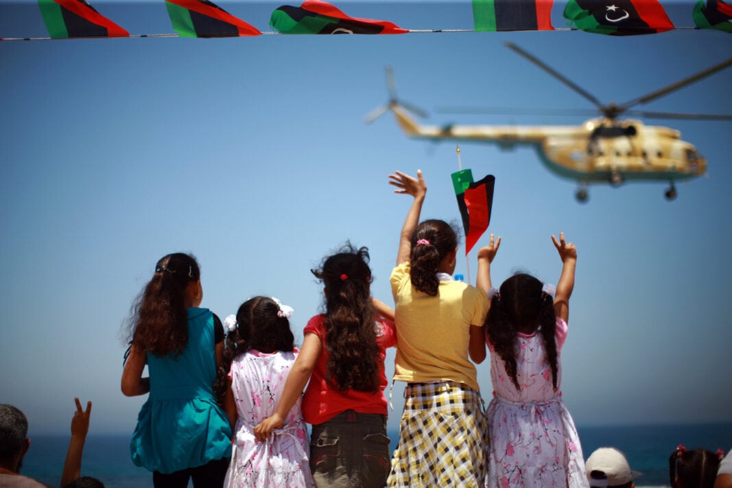 Zawiya, Libya, Celebrates One-Year Anniversary of Anti-Qadhafi Uprising Girls wave and flash victory signs at a passing helicopter during a military parade in the western city of Zawiya, Libya, held to mark the anniversary of an uprising last year that cleared the way for the anti-Qadhafi forces' march on Tripoli. Photo ID 516887. 11/06/2012. Zawiya, Libya. UN Photo/Iason Foounten. www.unmultimedia.org/photo/