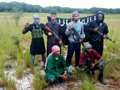 ISCAP-Mozambique fighters pose with weapons in front of the Islamic State Flag.
