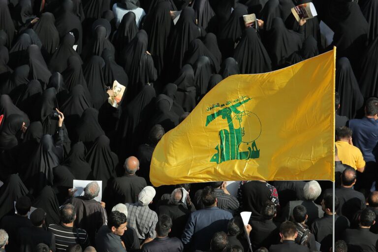 A crowd of people wave the flag of the Lebanese group Hezbollah in the street.