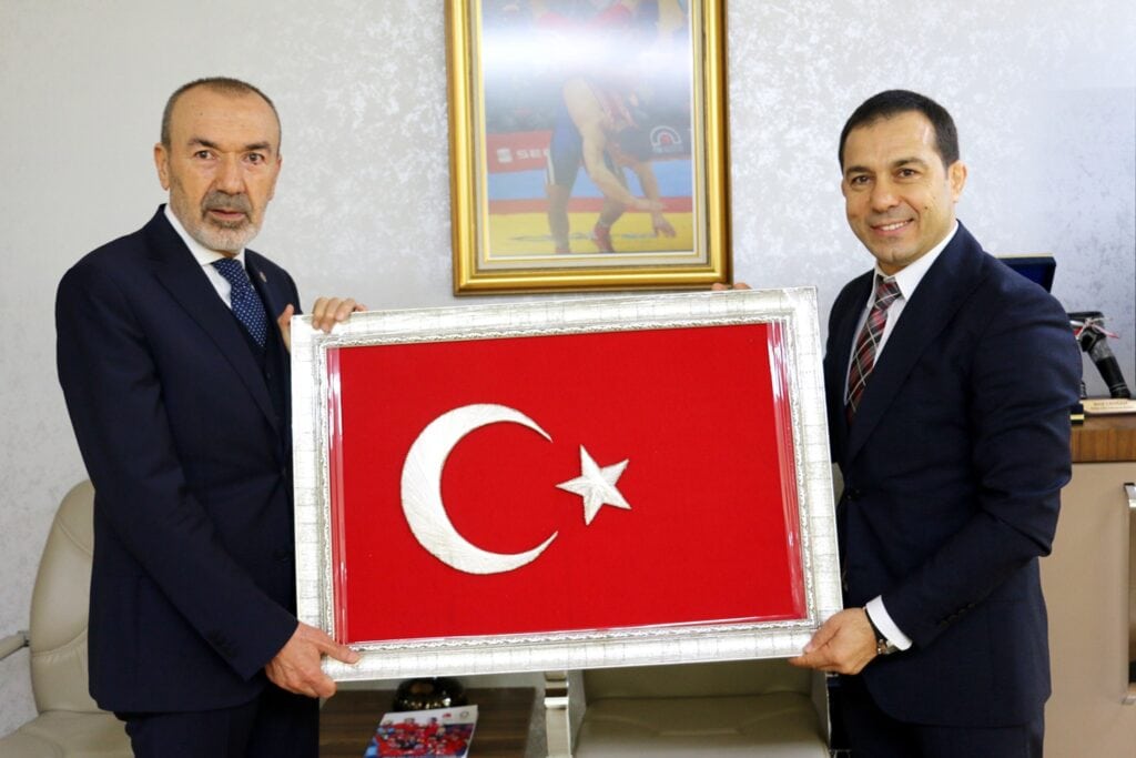 MHP Vice President Yasar Yildirim standing alongside Wrestling Association president Seref Eroglu. Both men are holding a flag of Turkey. 