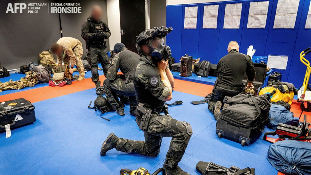 Five Tactical Response Team operators prepare for operation by equipping their plate carriers and helmet.