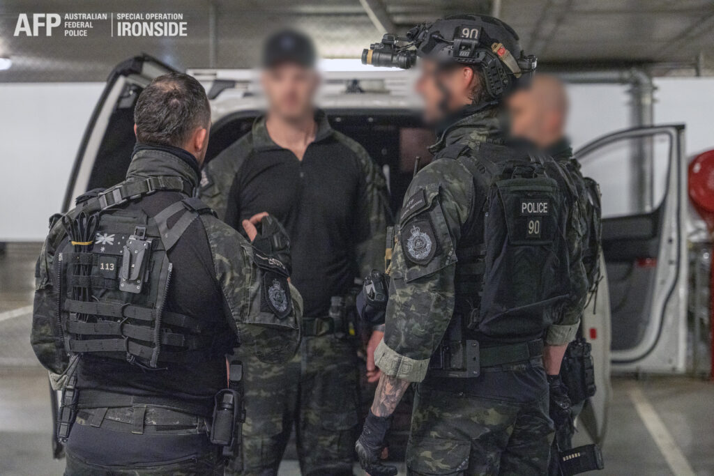 Three Tactical Response Team operators stand by the back of an open van in an underground car park during operation.