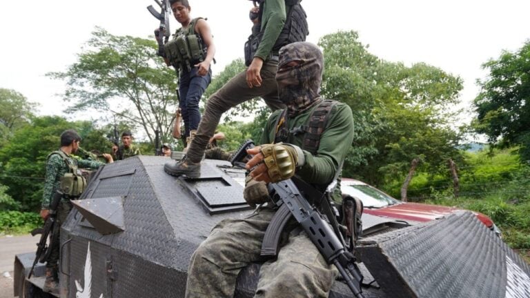 Militiamen armed with rifles on top of an armoured car.