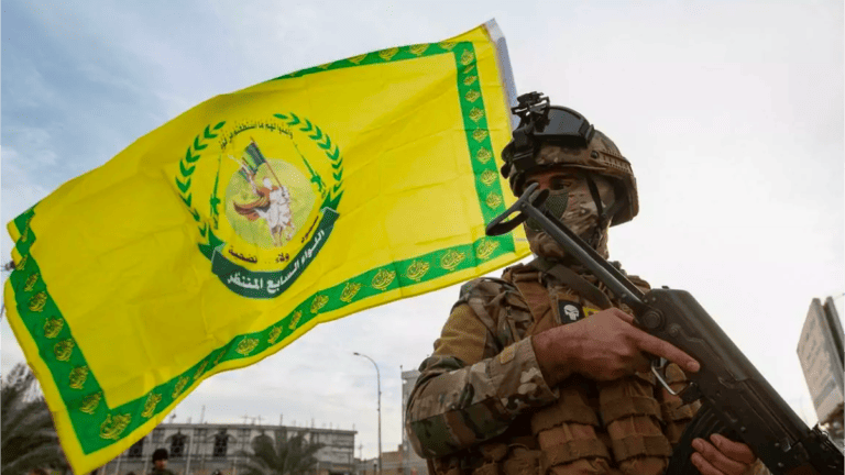 Kata'ib Hezbollah fighter in front of the organisations' flag.