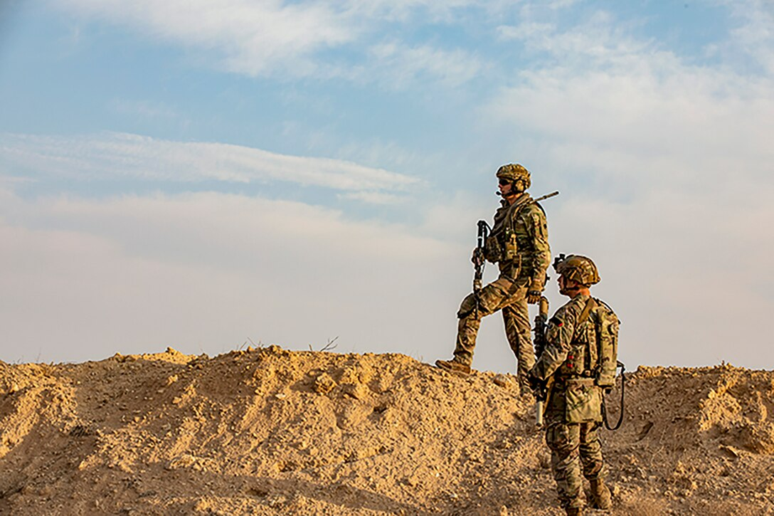 Two U.S. soldiers standing on a desert hill.