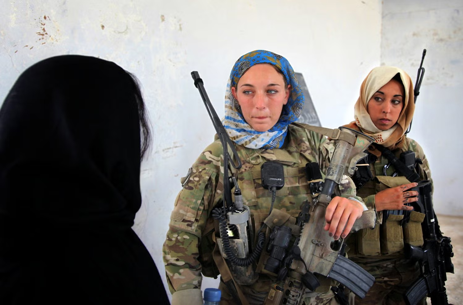 Two U.S. servicewomen in head scarves and combat gear speak with an Afghan woman during a Female Engagement Team visit in Afghanistan.